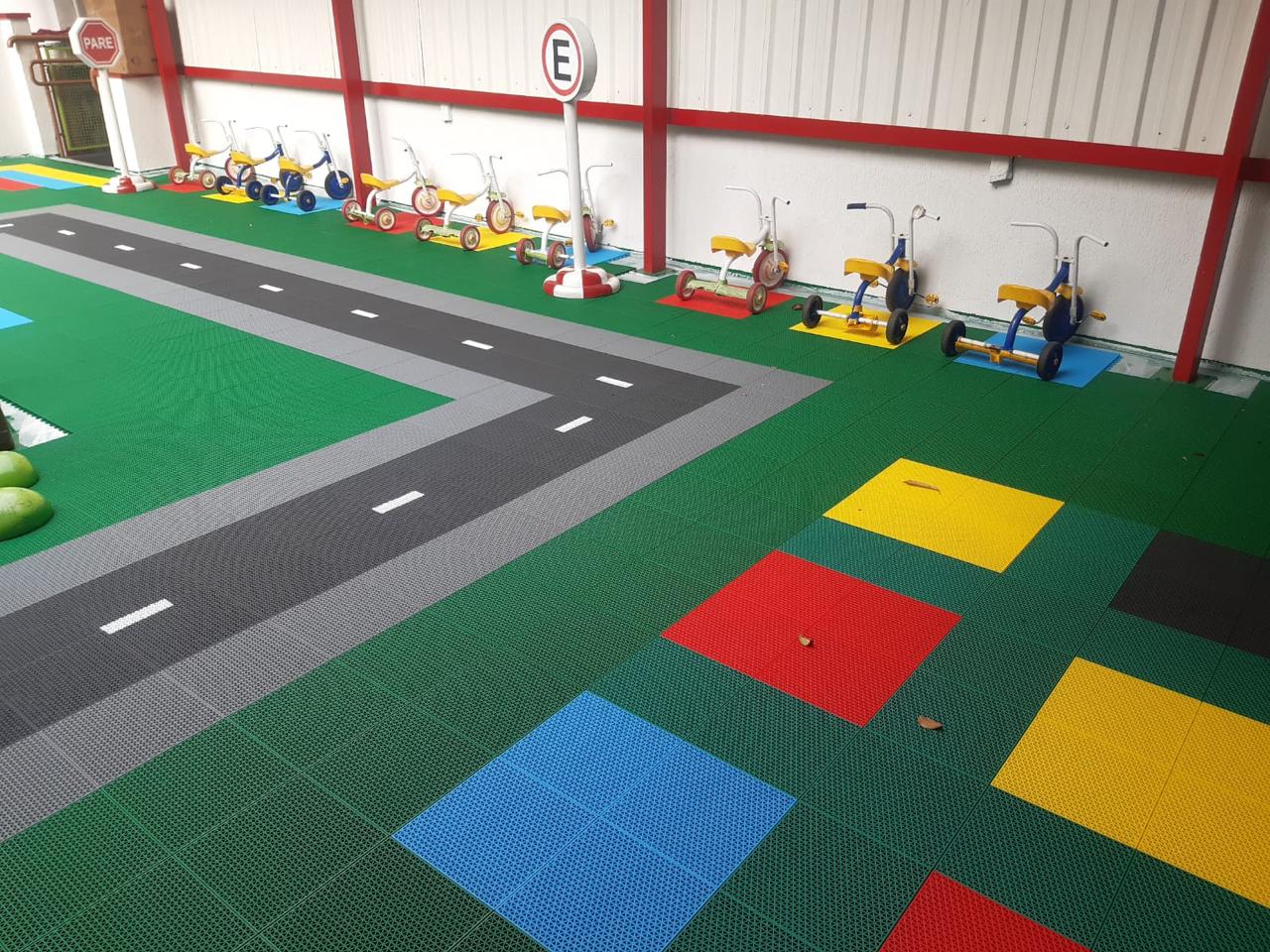 Pista de triciclos infantil com piso modular verde e faixa de asfalto